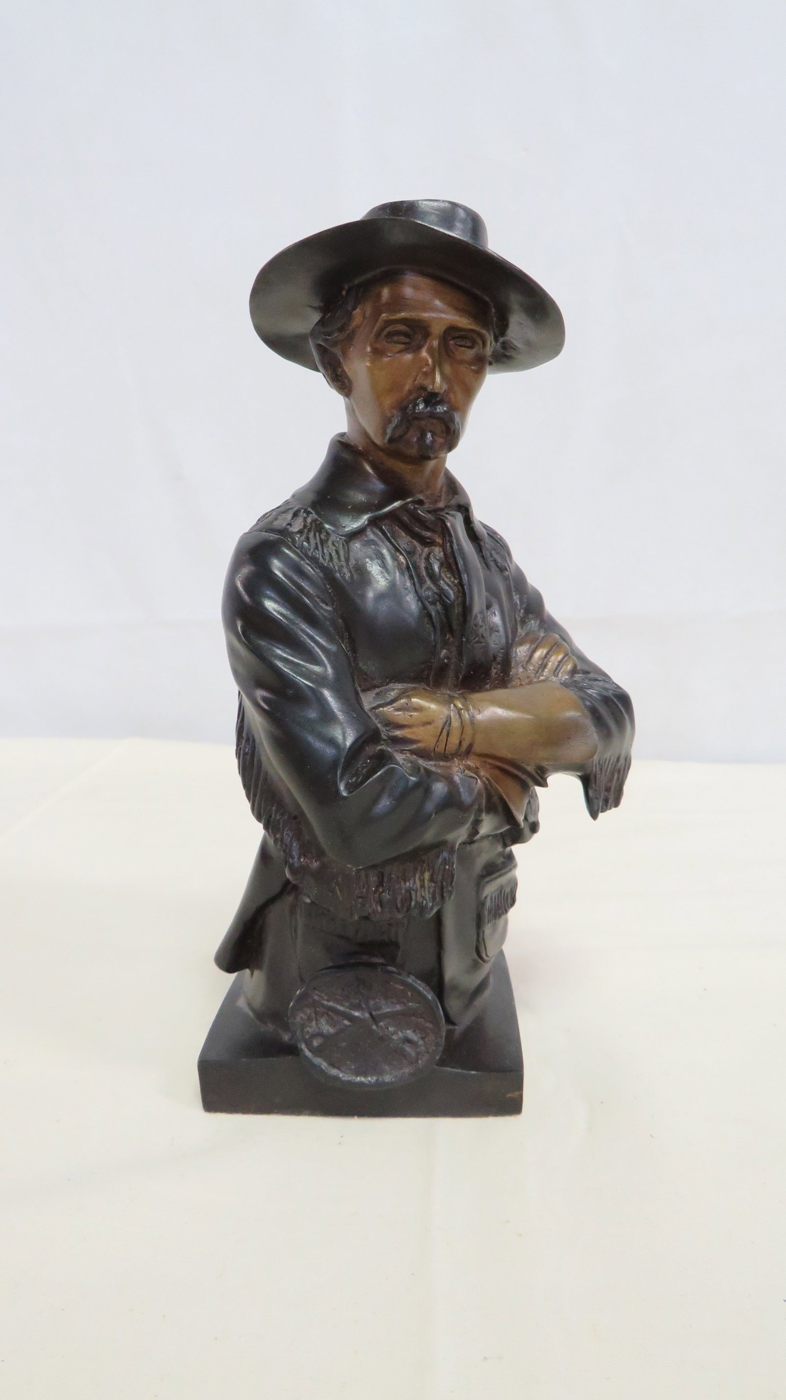 Western Lawman Cowboy Bronze Sculpture: Well executed figural bust depicting a mustached Old West frontiersman or lawman shown with arms crossed in a confident, authoritative pose. The base features a medallion with crossed swords motif. 8.