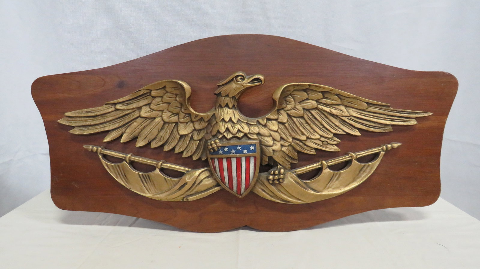 Mid Century Cast Iron Gilt American Eagle Plaque: Bold American patriotic wall plaque featuring a spread-wing eagle with red, white, and blue shield mounted on a shaped hardwood backboard. The eagle is cst iron with a gilt (gold-tone) finish, 