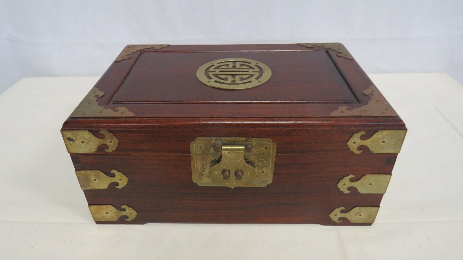 Vintage Chinese Brass Mounted Jewelry Box: Decorative Chinese hardwood chest featuring embossed brass corner mounts, hinges and lockplate, with central longevity medallion on the lid. 5.5"H x 12"L x 8"W