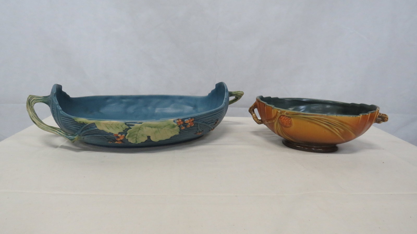 2 pc Roseville Pottery Pine Cone & Bushberry: 2 pc Roseville Pottery Pine Cone & Bushberry Console Bowls. Both have chips on inside top rim, but still make nice cabinet pieces. Bushberry Blue 417-14" 5"H x 18"L (with handles) x 9.5"W Pine Cone Br