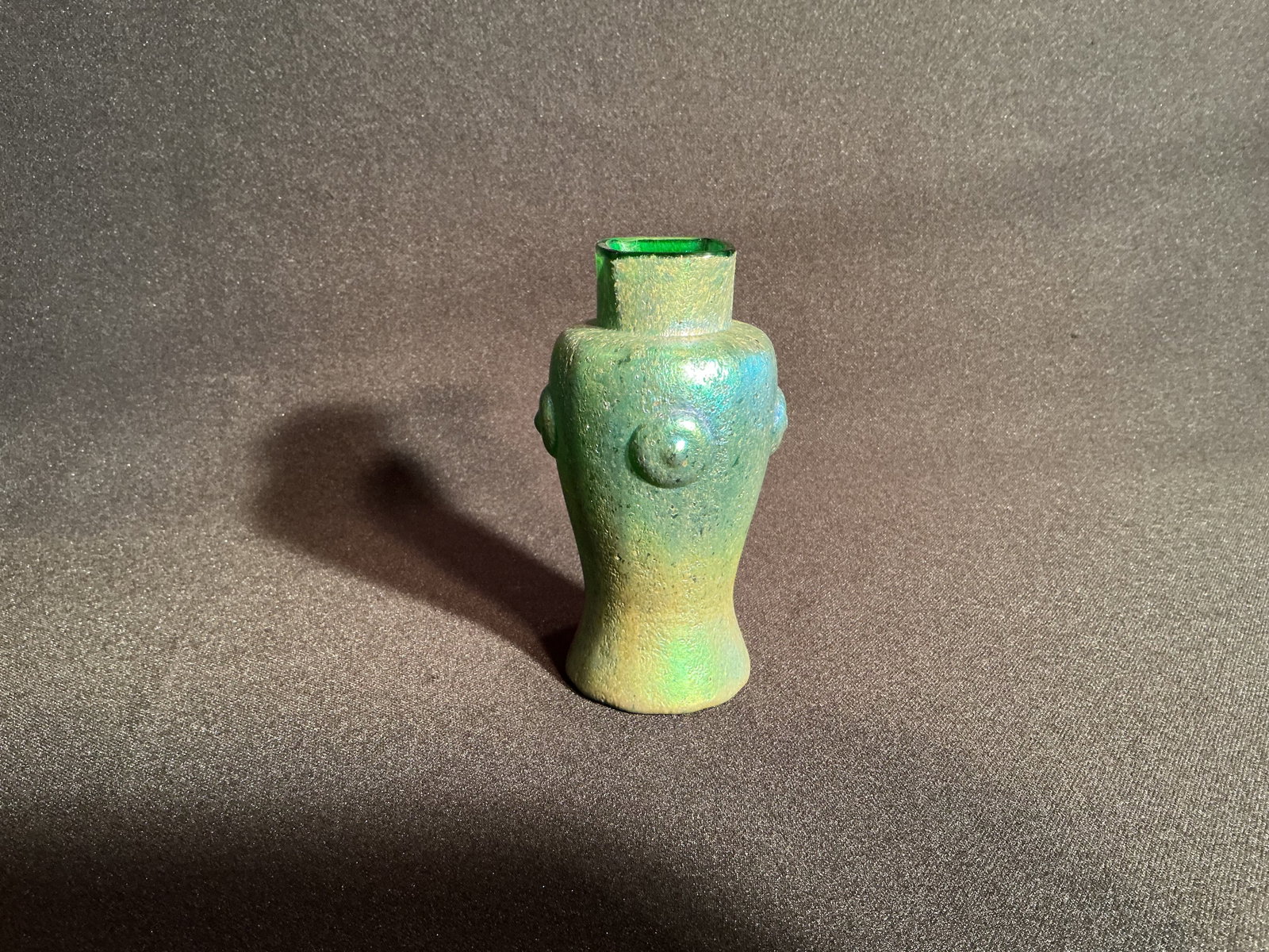 In the manner of Loetz Volcanic Green glass vase: Unmarked. Rich volcanic green glass vase with 4 round central medallion shaped designs on each side. The opening is squared in a dramatic collar top.