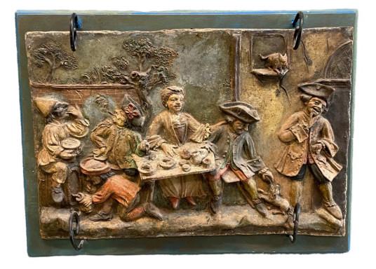 Polychrome Pottery Relief Plaque: Showing a lively Black Forest scene, mounted on blue painted board, paint and some clay loss throughout, surface dust, plaque 10H x 15W, board 12H x 16WLine Item # 68