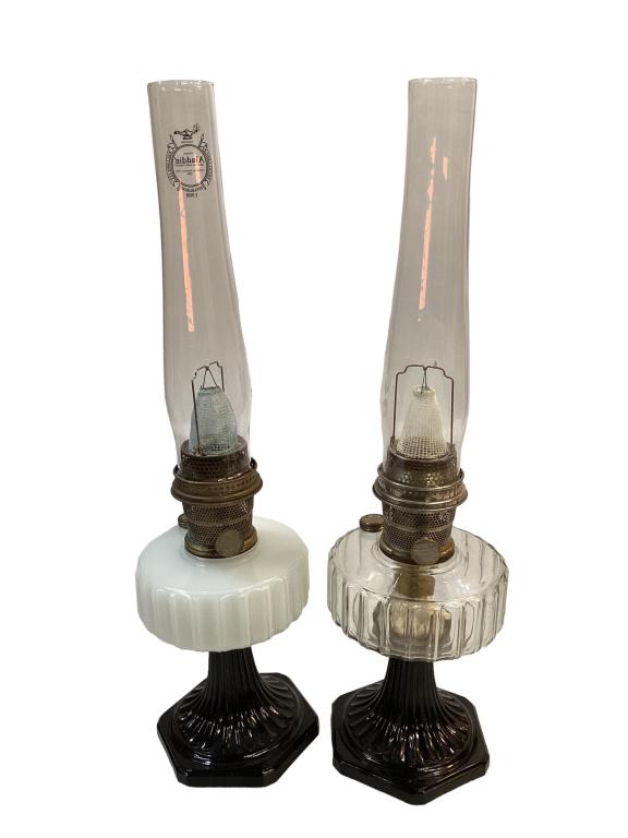 Two Aladdin Oil Lamps: Corinthian White moonstone font with black foot, new chimney, and a clear font with black foot, both adjustable wick knobs are marked