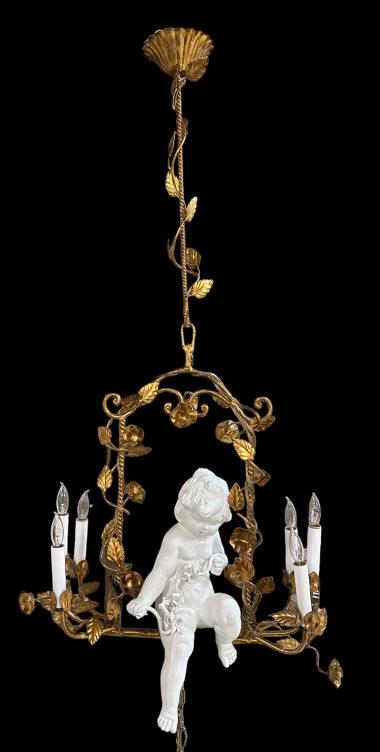 Hanging Italian Tole and Porcelain Cherub in Swing: 1960s, gilt metal swing with leaves and flowers, 3 lights on each side, porcelain cherub with crack to seat, 60 inch swag chain, 42H x 20W..surface dirt, tested and works