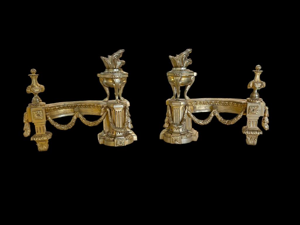Pair of Louis XVI Style Brass Chenet: Late 19th century..with flaming urns raised on hoofed feet, curved architectural plinth with draped floral swag, 11H x 12W inches..some surface wear Line Item # 37