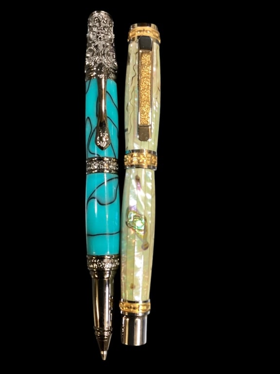 Two Artisan Crafted Ball Point Pens: 6 1/4 inch turquoise acrylic with ornate pewter cap and banding, mother of pearl with black veining, gold tone accents to clip and caps