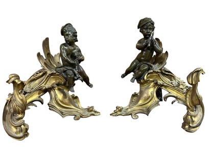 Pair of French Louis XV Style Chenets: Late 19th/20th century gilt and patinated bronze chenets with musical putto perched on an effortlessly scrolling base withfoliate decoration..age related wear and surface dirt, light corrosion and ver