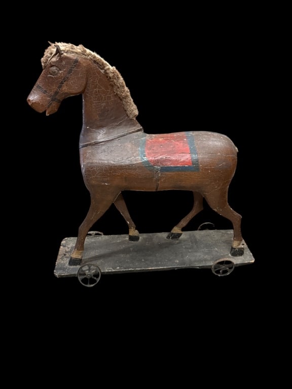 Antique Wooden Pull Toy Horse on Wheels: Charming late 19th c. hand-carved wooden horse pull toy on a four-wheel platform. Original painted surface with red saddle detail, animalhide mane, and iron-spoked wheels. 27 tall 27 long eight deep.