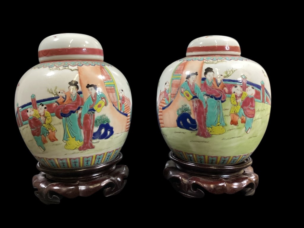 Near Pair Famille Temple Jars: Chinese porcelain ginger jars, a near pair with traditional Chinese symbols, depicting figures in courtyard, and playful setting. 8 inch jars hand decorated with matched wooden stands, red seal chop m