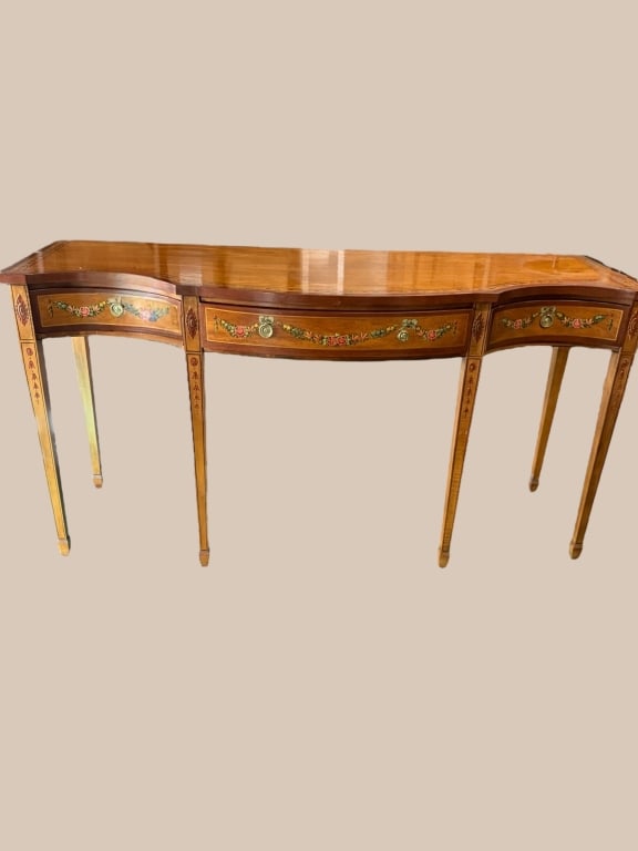 Hand Painted Sideboard in the Hepplewhite Style: Elegant Hepplewhite-style satinwood demilune sideboard with hand-painted floral swags, ribbon motifs. Features a bowed front with three drawers and tapered square legs, 36 tall 70 wide 24.5 deep
