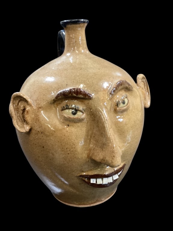 Southern Folk Art Face Jug: Don Craig sculpted face jug with prominent nose, shaped eyebrows, eyelashes and small ears. A whimsical female face jug, with China plate teeth. Script signed to base. 12 inches tall