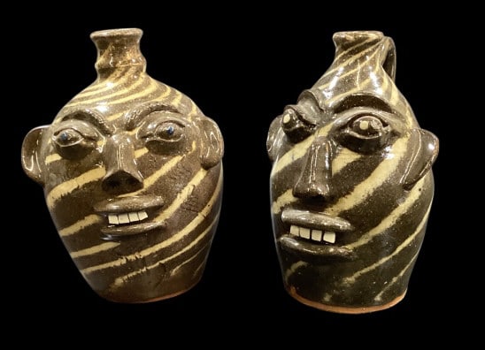 Two Walter Fleming Face Jugs: 9 inch swirl face jug with bug eyes, big lips and chip teeth. 10 inches tall swirl jug, with same facial features. Both with good color, both signed