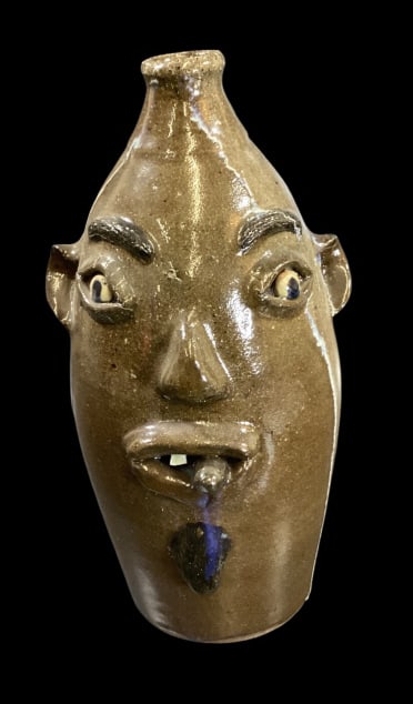 Billy Henson Stoneware Face Jug: Tall tapered form jug, wood fired, 14.5 inches tall, alkaline glazed with drip trail. Cigar man with busy brows, goatee, one chip tooth and cigar stub. Signed and dated 1997