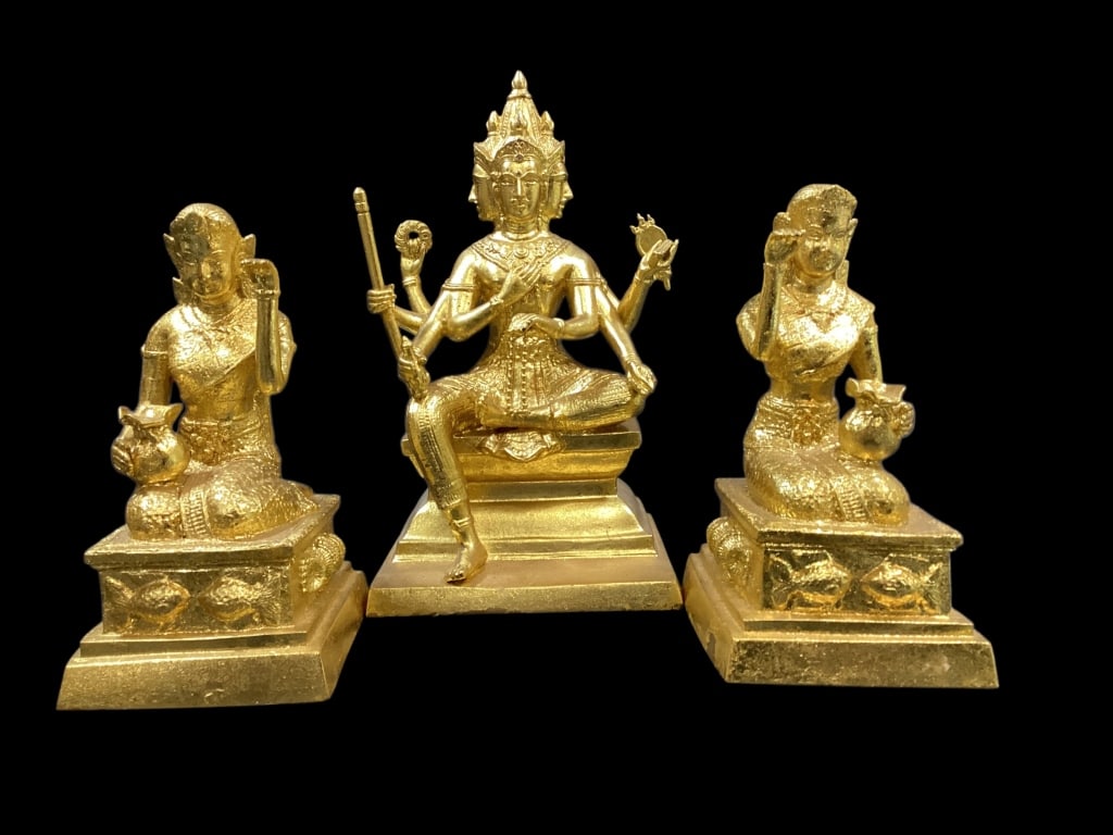 Brass Statue of Brahma with Nang Kwak: Three Gold washed statues. The central figure is Brahma, Hindu God of creation, four faced god, with 8 arms, seated on Dias. Right and left pair of 8.5 statues representing Nang Kwak, or the beckoning