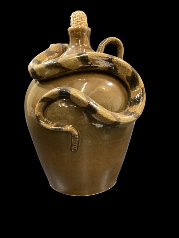 Otis Norris Rattlesnake Jug: Southern Carolina Artist Otis Norris hand crafted stoneware jug with applied rattlesnake. Dark olive green to brown alkaline glaze on a 14 inch bulbous body. Loop handle, spout with an added corn