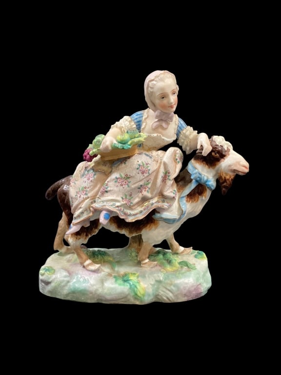 Meissen Porcelain Figural: Depicting a young woman, riding a goat. Carries a basket of vegetables. The goat with a blue neck bow. 9 x 10 inches, pastel colors, lovely facial details. Meissen blue stamp mark