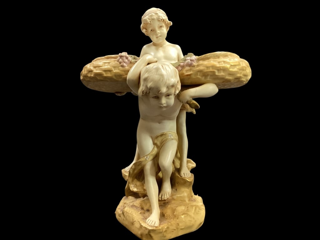 Royal Dux Porcelain: From Art Nouveau period, features Puti support or ting a basket. Characteristic of the Bohemian factory with matte finish and delicate polychrome accents. 12 inches tall, bears pink triangle mark to