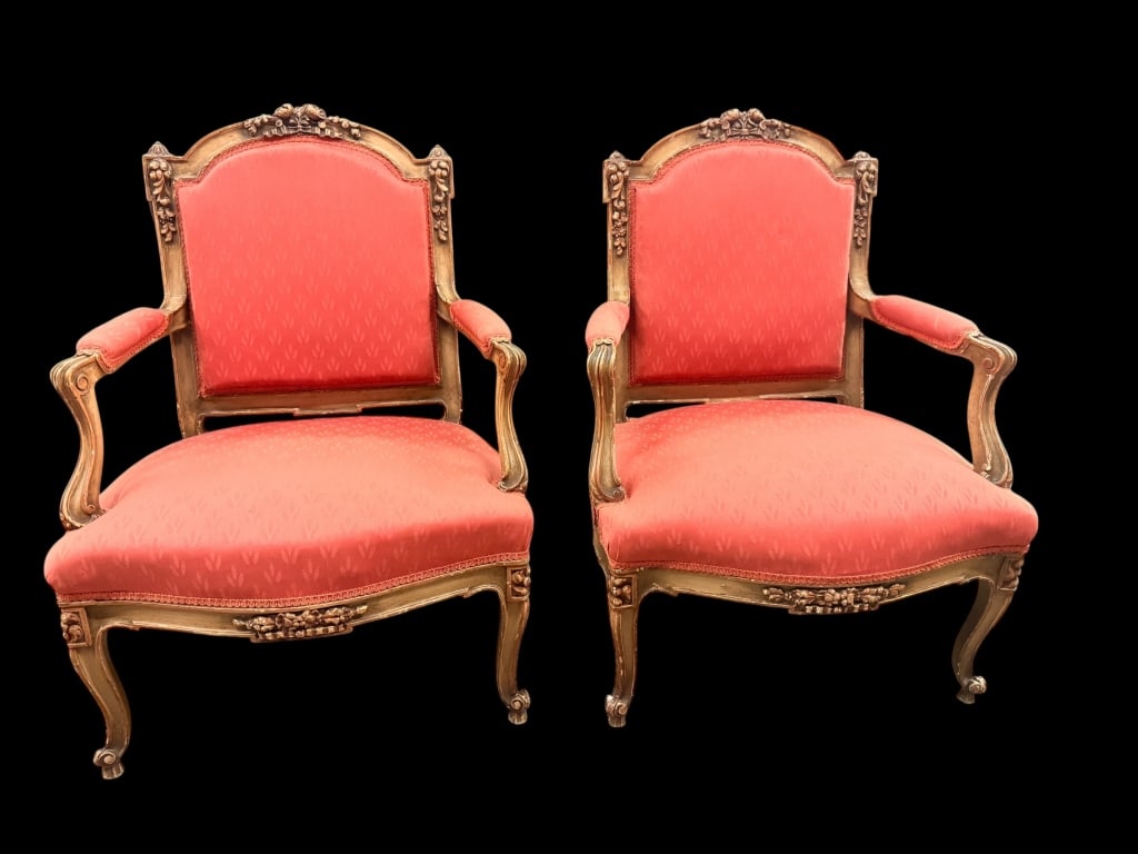 Pair of Louis XV Style Giltwood Armchairs: A striking pair of Louis XV style giltwood bergère-style armchairs upholstered in a vibrant coral-red fabrication with a subtle repeating stylized leaf motif. The elegantly molded frames boast