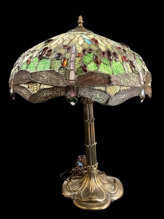 Tiffany Style Table Lamp: Tiffany Style Table Lamp Dragonfly pattern leaded glass shade, with multiple jewel like cabochons. The Deco style base of metal with a bronze gold finish, in natural form with reeded column and petal 