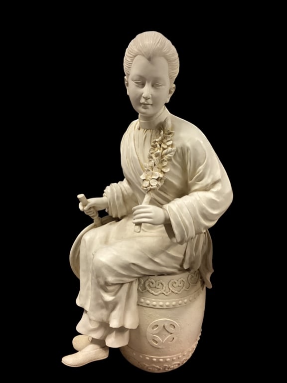 Ceramic Sculpture of Asian Woman: Export decorative figure, depicting a seated female figure, on a drum shaped stool, holding a floral spray, traditional robes, serene facially expression. Reminiscent of blanc de chine, constructed
