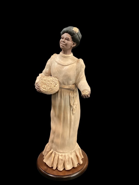Hand Crafted Sculpture: Attribution to Cairn Studio, this 21 inch figure of a Black woman in long dress, holding a basket of roses, with single rose in left hand. Signed To Thomas, ?04. Mounted on a wooden base