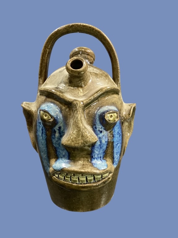 Randy Tobias Southern Folk Pottery: Folk Art stoneware weeper jug, with blue glaze runs at eyes, double row clay teeth, over top loop handle, double spout field jug, 12 inches tall, green alkaline glaze. Signed in body.