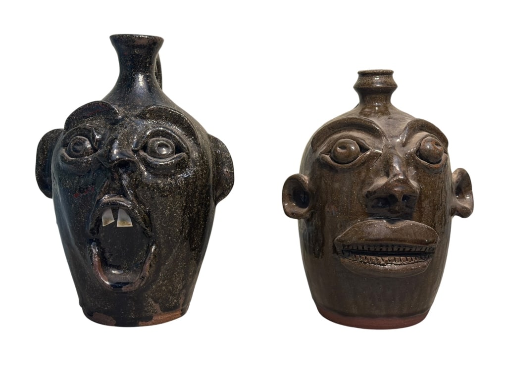 Two Marvin Bailey Face Jugs: Two Southern folk art face jugs by Marvin Bailey. The left "Two-Tooth" jug features a dark charcoal-black glaze, deeply set eyes, a pinched nose, and a wide-open screaming mouth with two large white p
