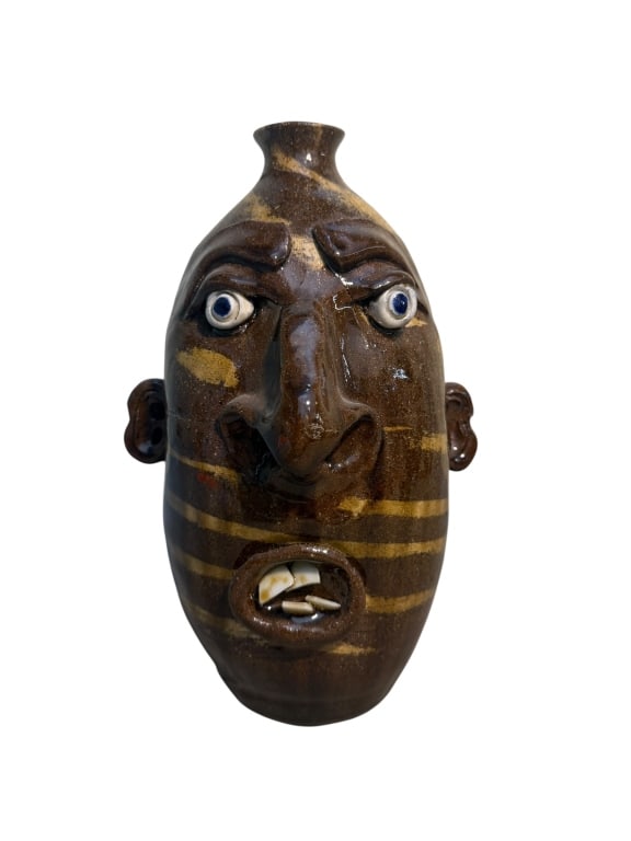 Mike Henning Face Jug: Southern folk art face jug by Georgia potter Mike Henning. The jug features a glossy brown alkaline glaze with lighter tan swirl bands running across the body. Its elongated form has a narrow neck, fu