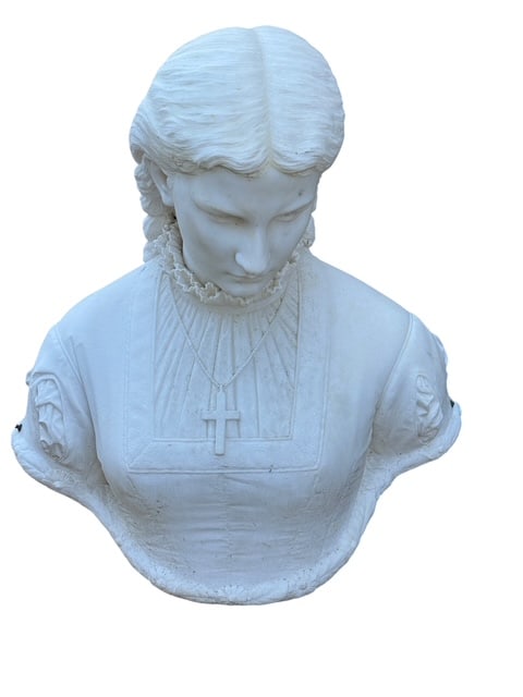 Carved White Marble or Alabaster Bust: Carved white marble or alabaster bust of a young woman wearing a high-collared, lace-trimmed dress and a simple crucifix pendant. Her braided hair, softly modeled features, and devotional necklace ref