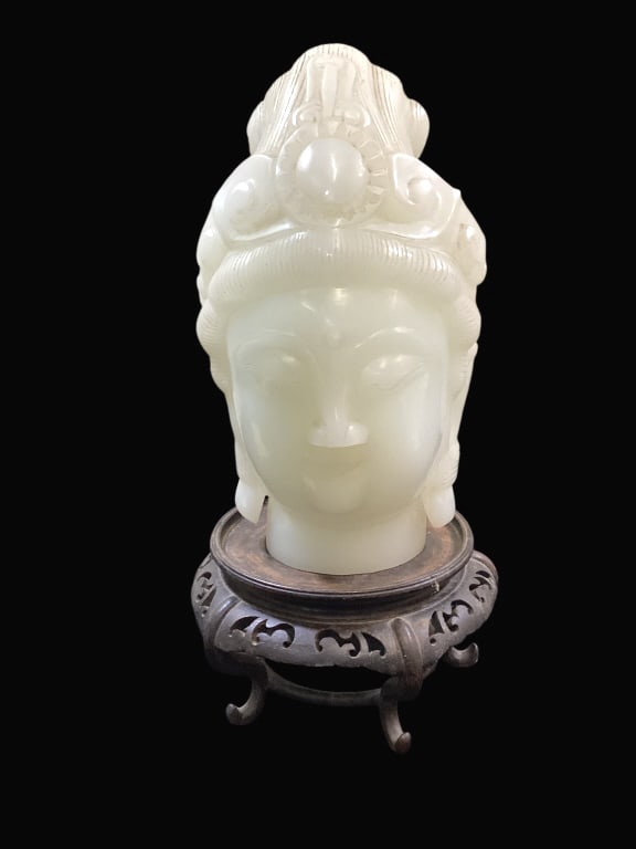 Carved Bust of Guanyin: Chinese carved bust of Goddess Guanyin, 11 inches tall, of creamy white color glass. Displaying an elaborate headpiece and hair, elongated ears. Face in repose. With a footed Asian wood display stand