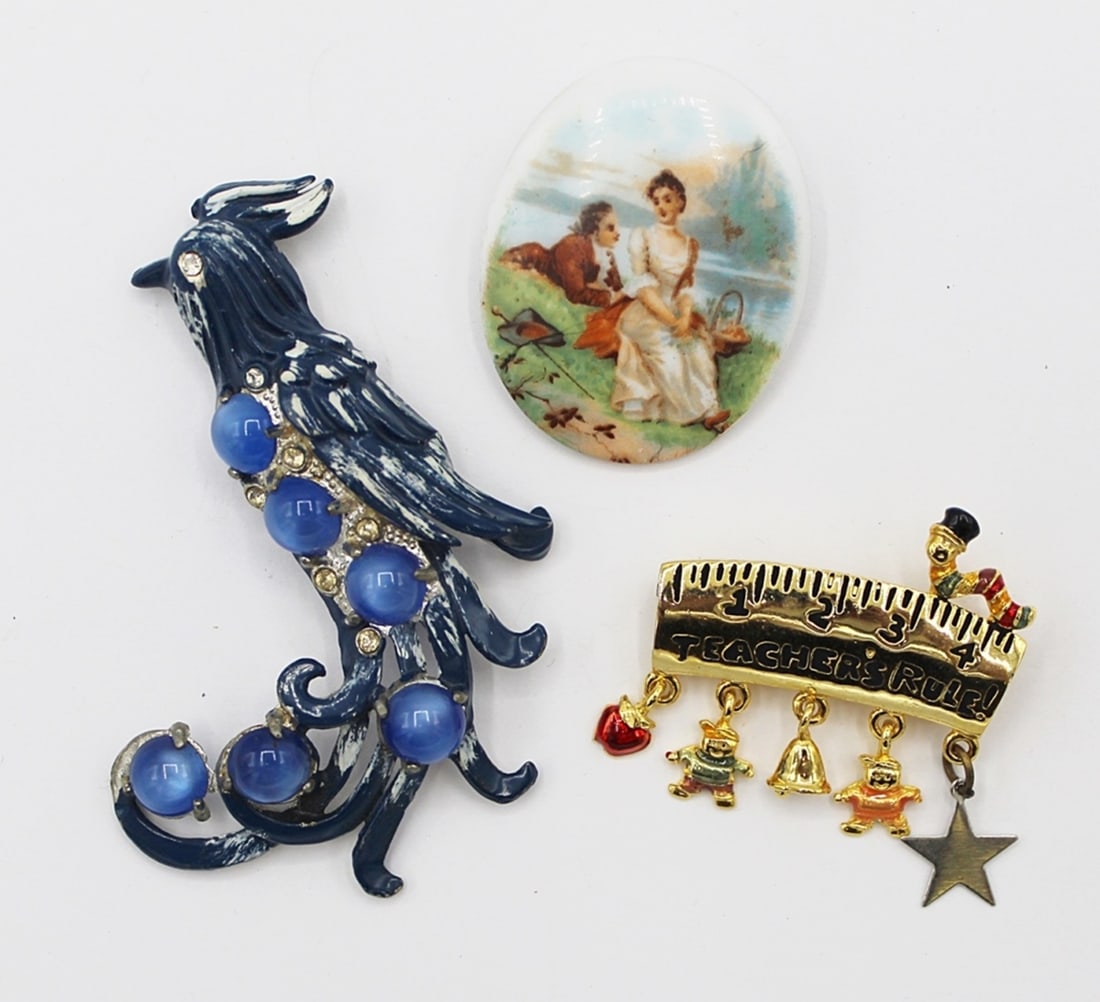 3 VINTAGE BROOCHES: VINTAGE MOONSTONE BIRD BROOCH, VINTAGE PAINTED SCENE BROOCH AND VINTAGE GOLD TONED DANECRAFT SIGNED "TEACHERS RULE!" BROOCH. ESTIMATE: $50-$75