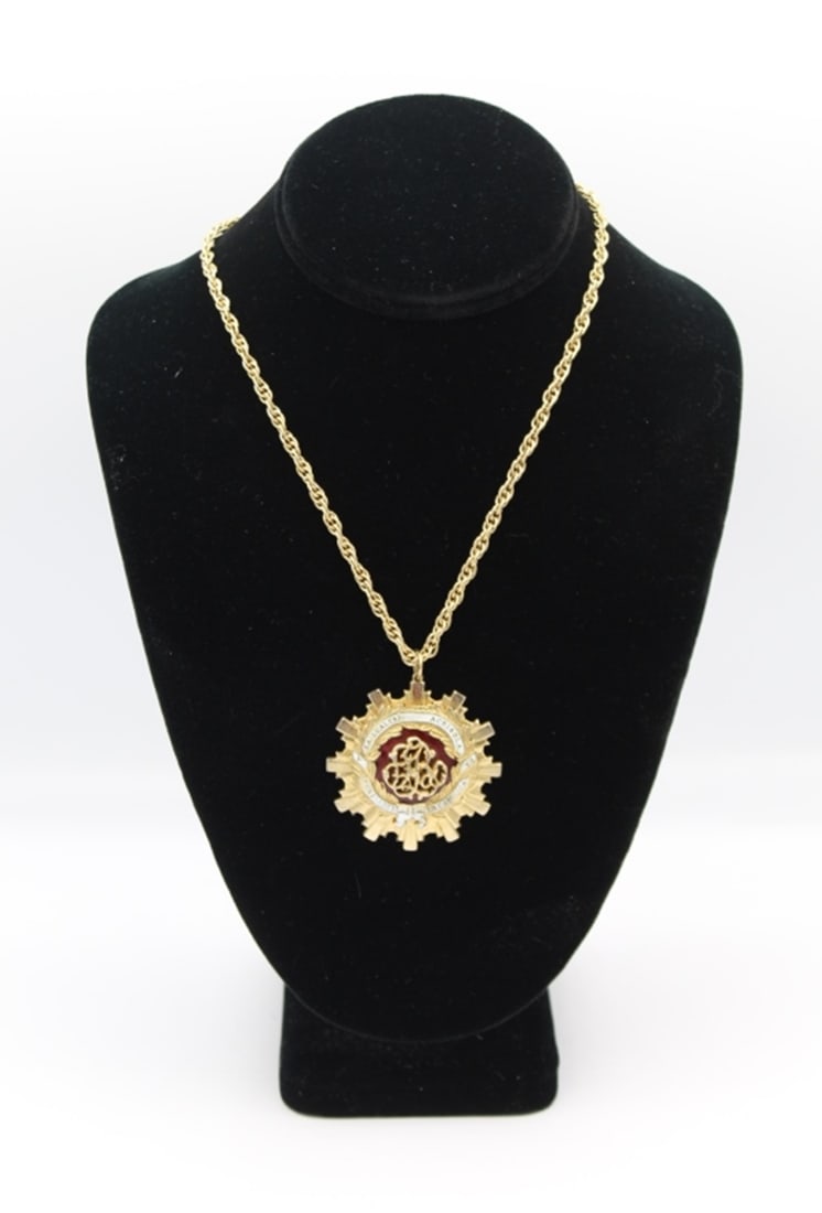 SIGNED CORO NECKLACE: GOLD-TONED WITH RED ENAMEL PENDANT. PENDANT READS "LEALTAI ACRISOLA POR ISABEL LA CATOLICA". 18" CHAIN. ESTIMATE: $50-$75