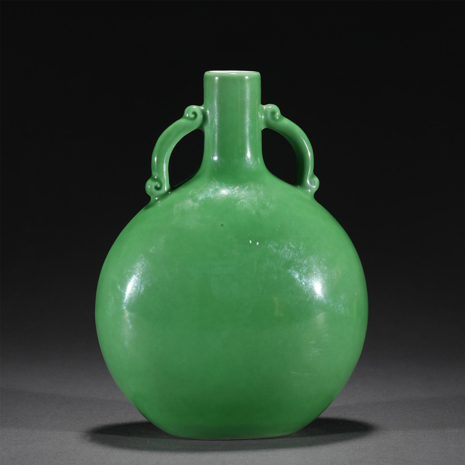 A GRREN GLAZE PORCELAIN FLASK MOON VASE,QIANLONG: A GRREN GLAZE PORCELAIN FLASK MOON VASE,QIANLONG The flattened globular body rising from a rectangular foot to a flared neck flanked by a pair handles, covered in green glaze, qianlong six characters 