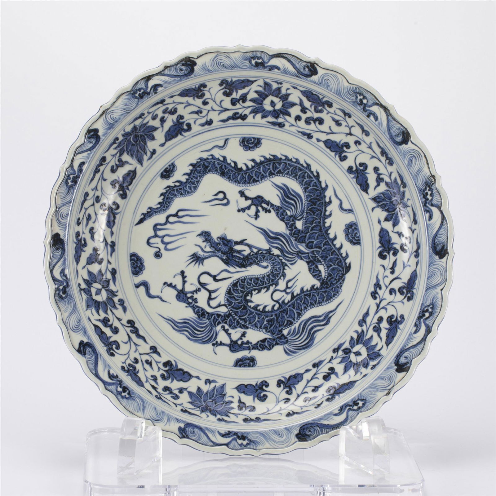 A BLUE AND WHITE PORCELAIN DISH: A BLUE AND WHITE PORCELAIN DISH The dish has rounded sides and an inverted rim, and is decorated in the center with four-claws dragon encircled with floral scrolls. Dimension: Diam. 44 cm. H. 7 cm. We