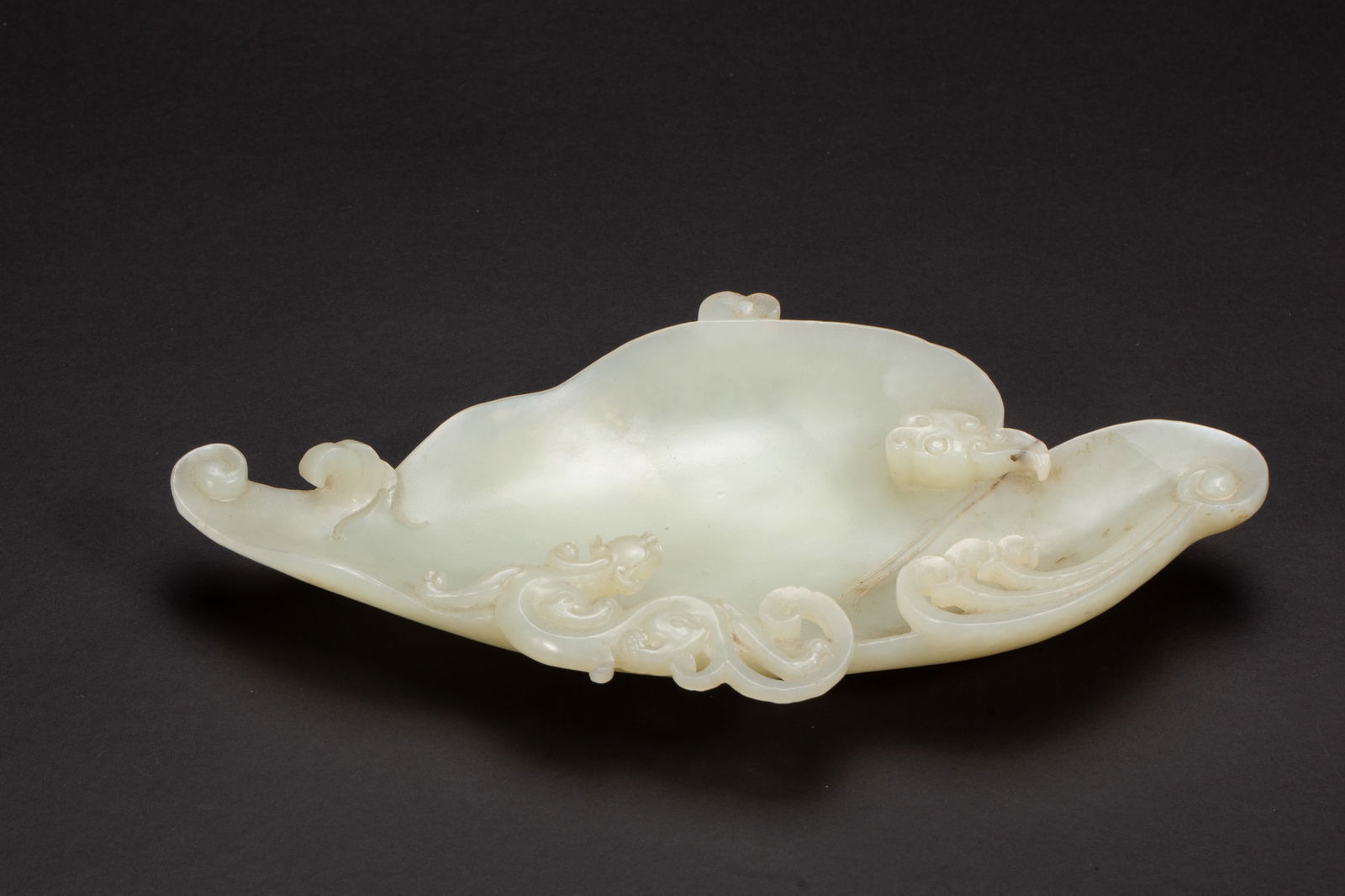 A CARVED WHITE JADE INKWELL: A CARVED WHITE JADE INKWELL The concave vessel flanked with a chilong at the side, the stone is of evenly white tone with russet speckles. Dimension: L. 15.5 cm. W. 8 cm. H. 2 cm. Weight 120 grams.