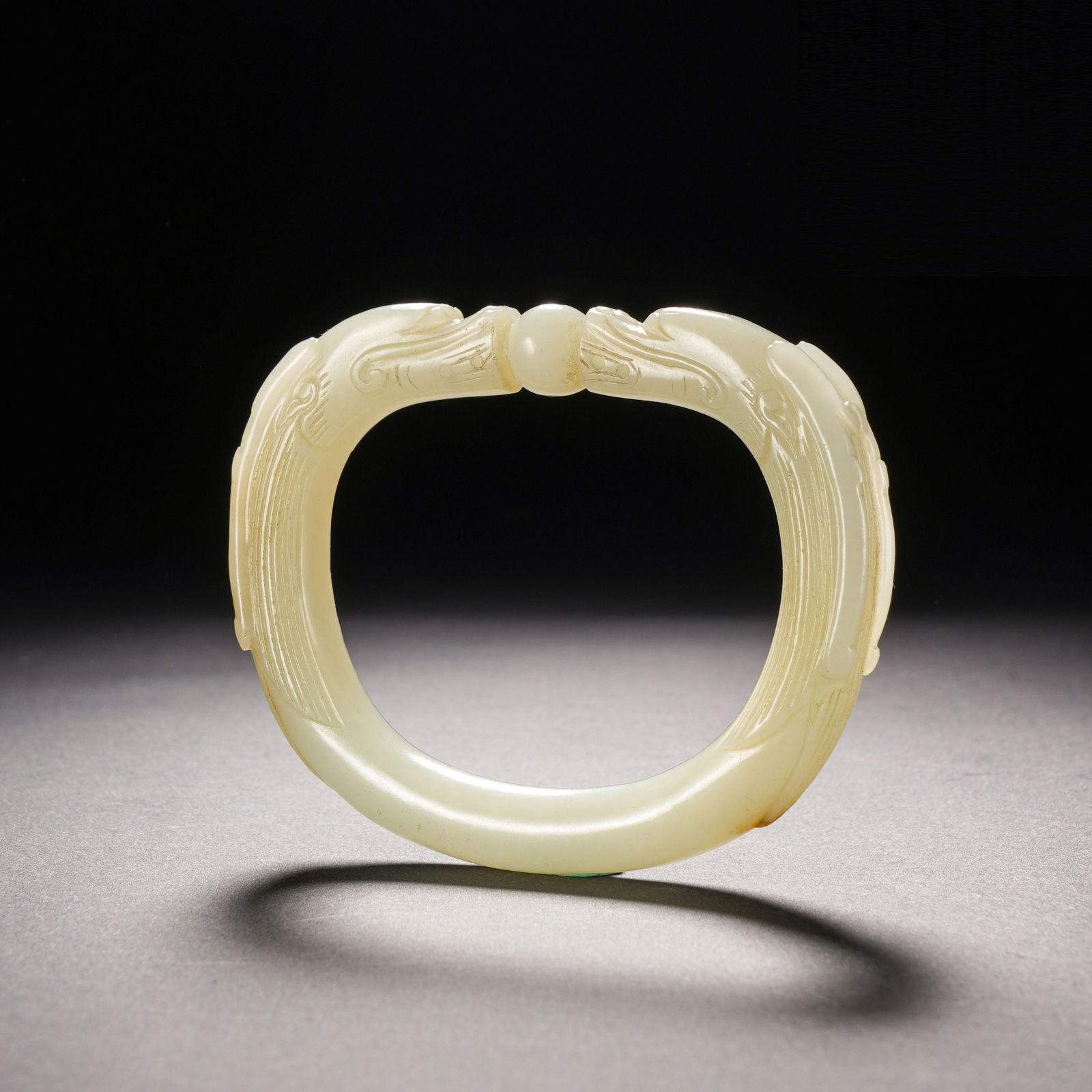 A CARVED WHITE JADE DRAGONS BANGLE: A CARVED WHITE JADE DRAGONS BANGLE The cylindrical jade band of white colour, terminated with dragon heads and well polished. Dimension: 6x4.5-8.2x6.5 cm. Weight 55 grams.