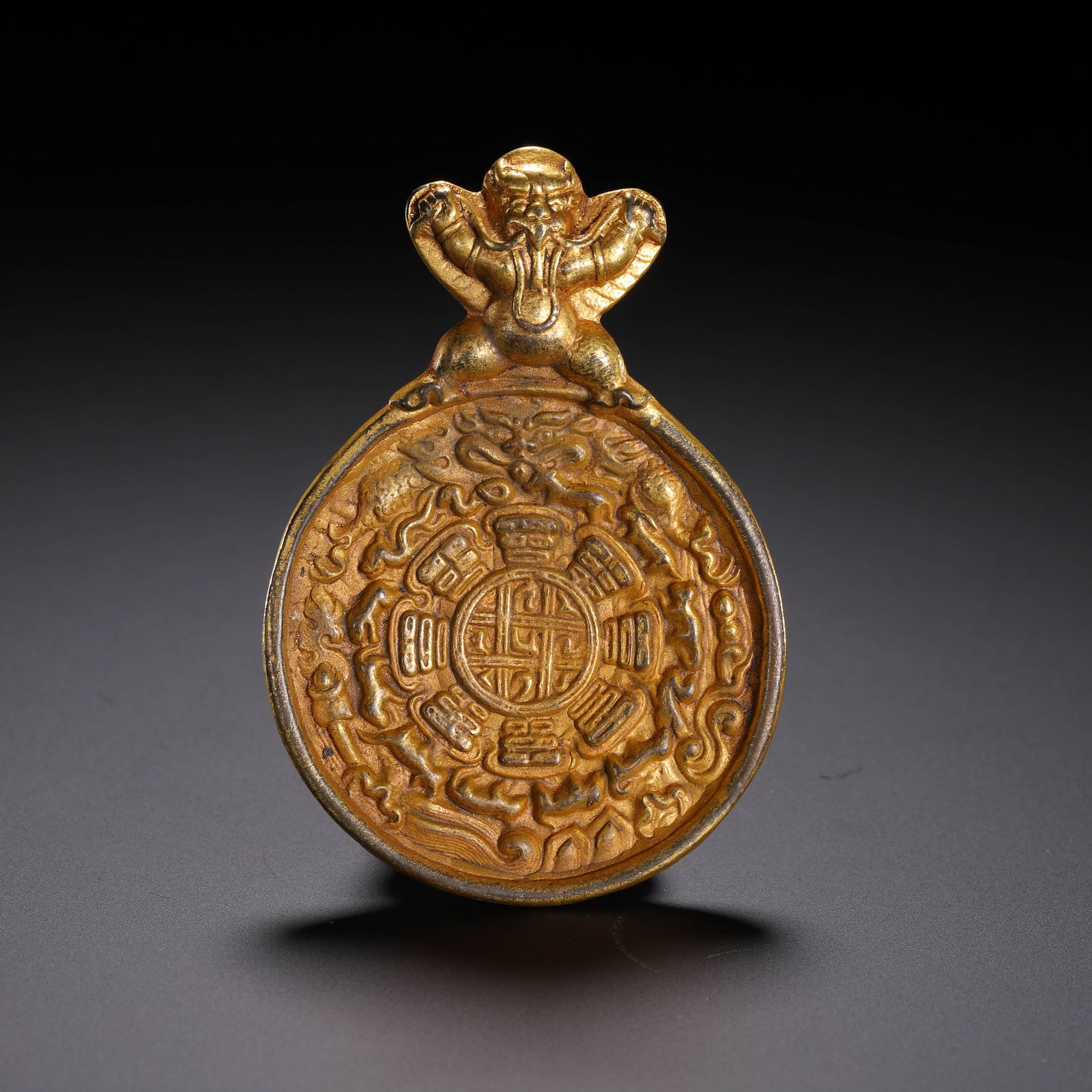 A TIBETAN BRONZE-GILT AMULET: A TIBETAN BRONZE-GILT AMULET Oval form Tibetan buddhist amulet pendant, richly gilt. Dimension: L. 7.5 cm. W. 5.5 cm. Weight 60 grams.