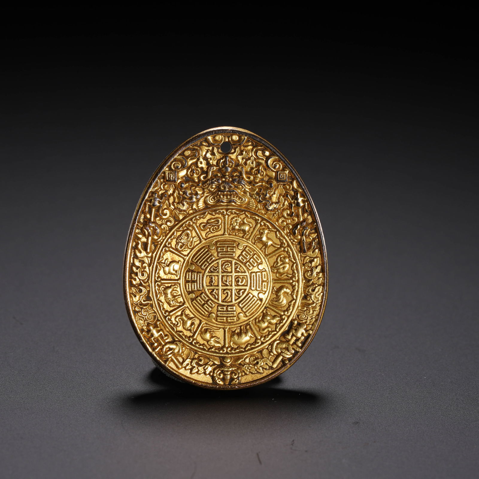 A TIBETAN BRONZE-GILT AMULET: A TIBETAN BRONZE-GILT AMULET Oval form Tibetan buddhist amulet pendant, richly gilt. Dimension: L. 4.5 cm. W. 3.5 cm. Weight 40 grams.