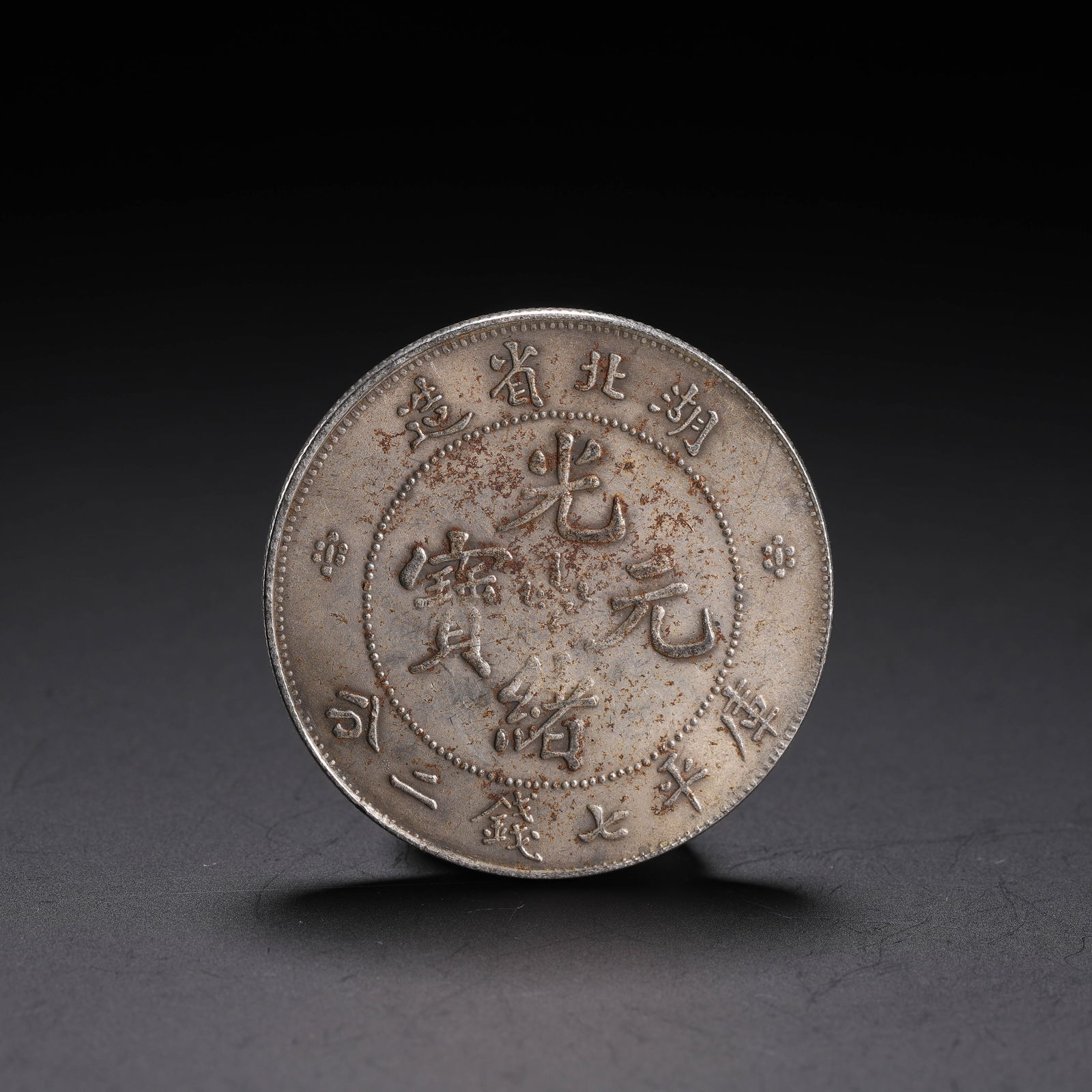A CHINESE SILVER COIN: A CHINESE SILVER COIN Of flatten circular shape, edge grained, with oxidize surface marks. Dimension: L. 4 cm. W. 4 cm. Weight 20 grams.