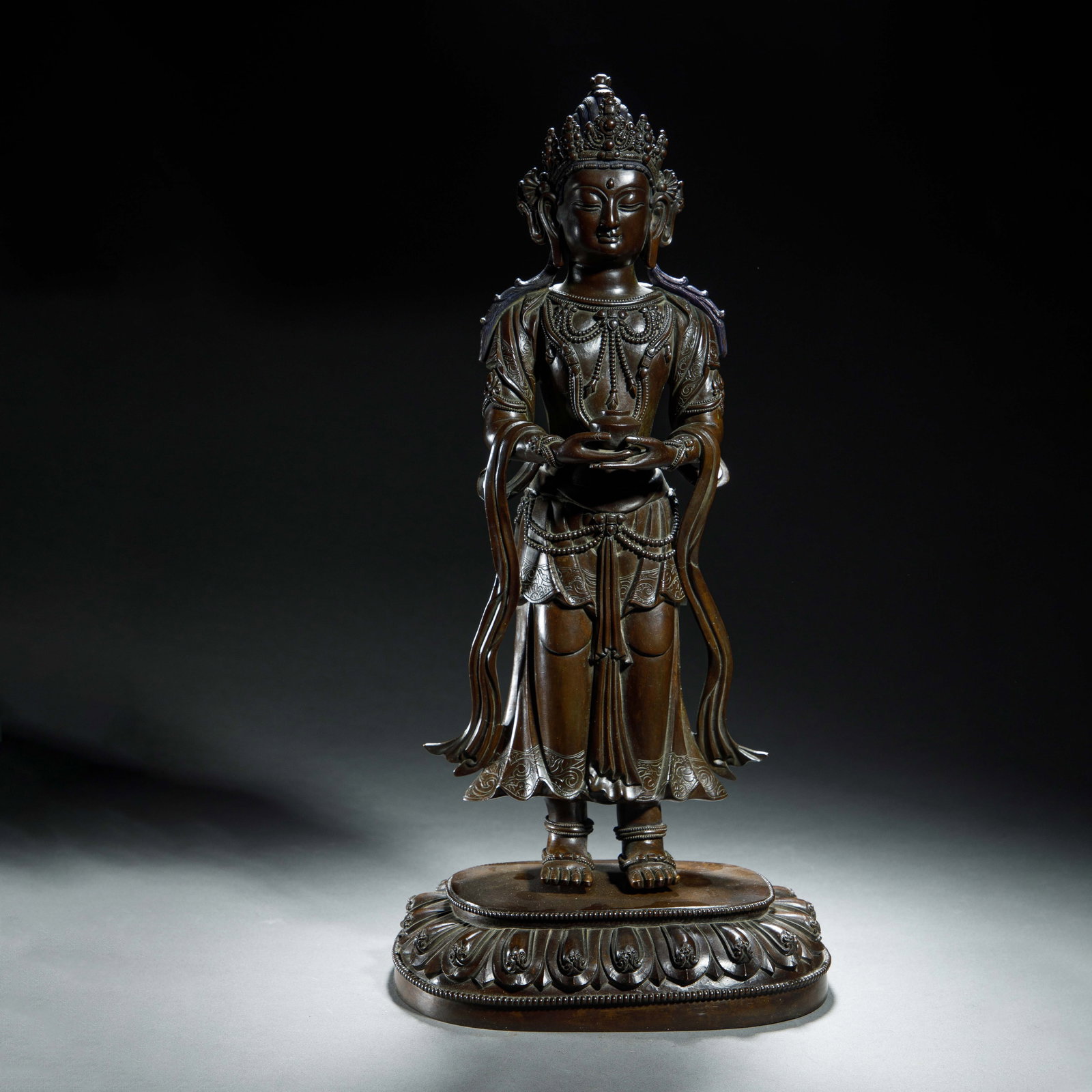 A BRONZE STANDING BODHISATTVA: A BRONZE STANDING BODHISATTVA His hair is swept back into a topknot beneath the crown, and long plaits cascade down the shoulders. The face has downcast eyes and a serene expression. The deity wears b