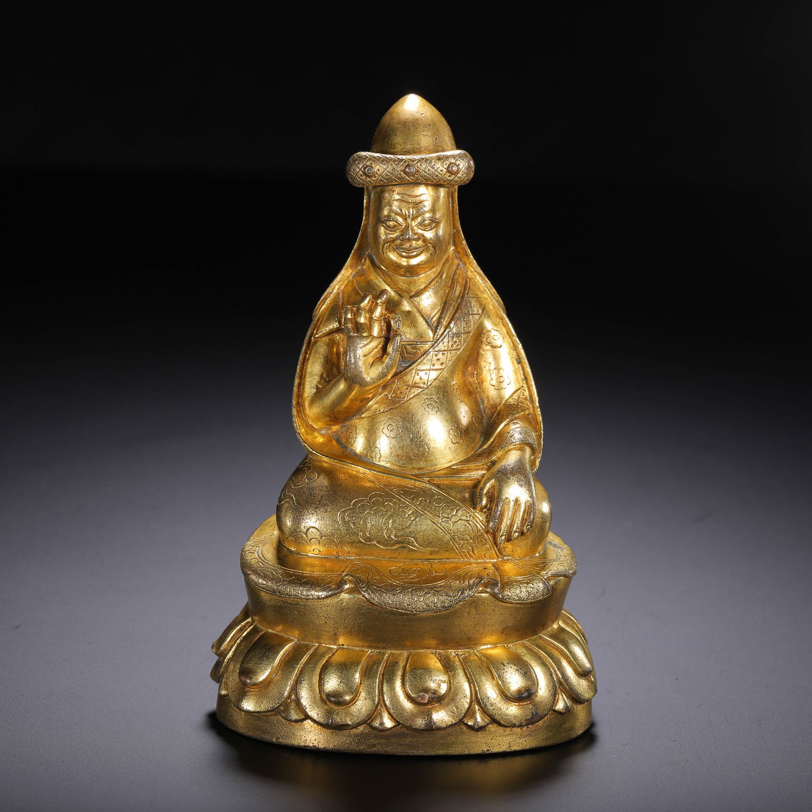 A BRONZE-GILT SEATED MASTER: A BRONZE-GILT SEATED MASTER Seated in dhyanasana in single lotus base, clad in heavy robe, adorn with hat, richly gilt. Dimension: H. 12 cm. Weight 450 grams.