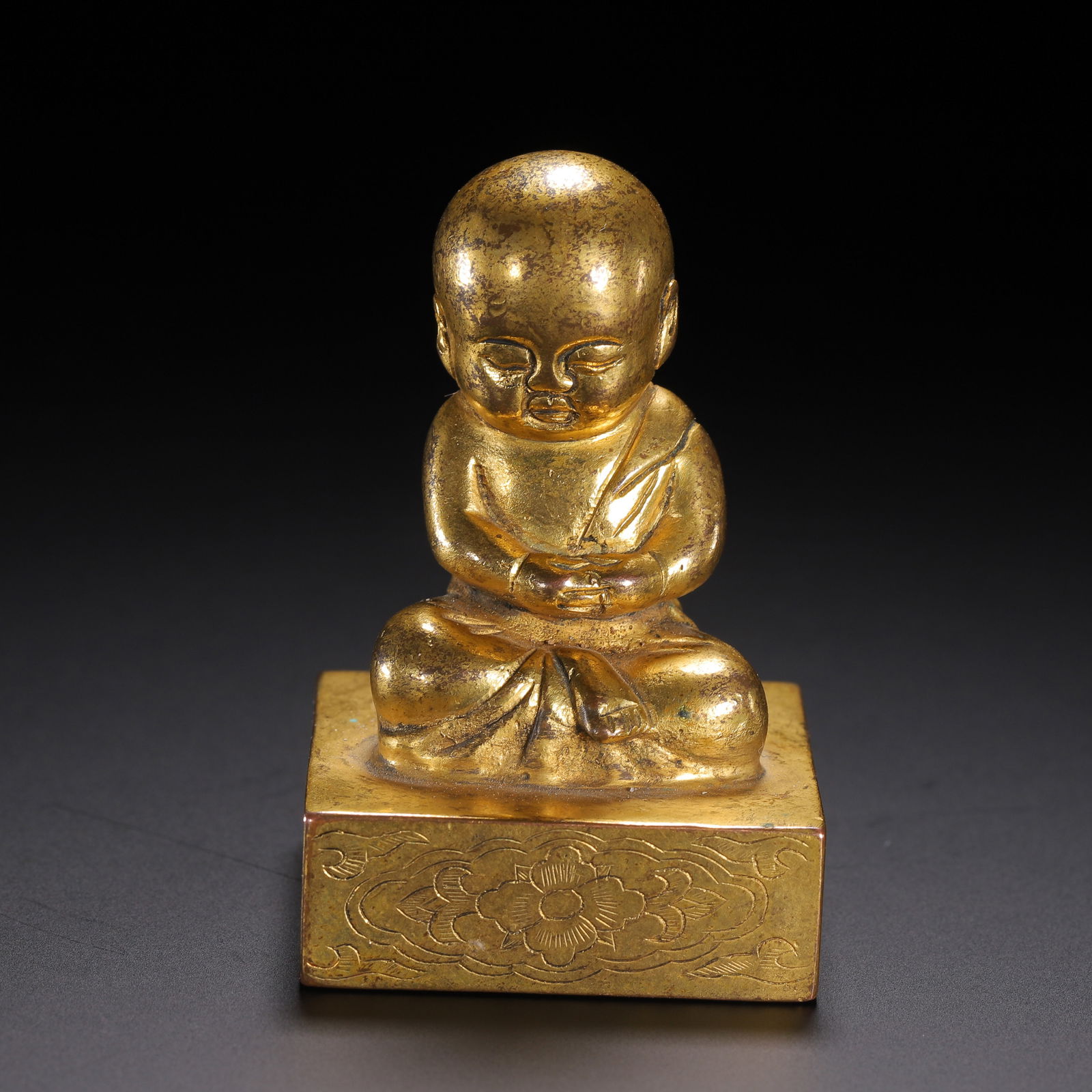 A BRONZE-GILT MONK SEAL: A BRONZE-GILT MONK SEAL The squared seal surmounted with a monk, richly gilt. Dimension: L. 4 cm. W. 4 cm. H. 6.5 cm. Weight 300 grams.