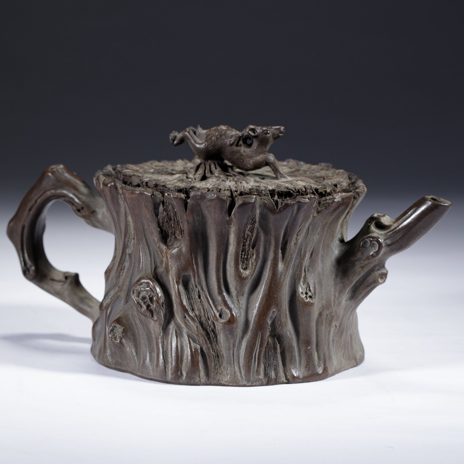 CHINESE YIXING ZISHA TREE-FORM TEAPOT: CHINESE YIXING ZISHA TREE-FORM TEAPOT This striking Chinese Yixing Zisha teapot measures 21 cm in length, 11.5 cm in width, 10 cm in height, and weighs 591 grams. It is masterfully sculpted to mimic a