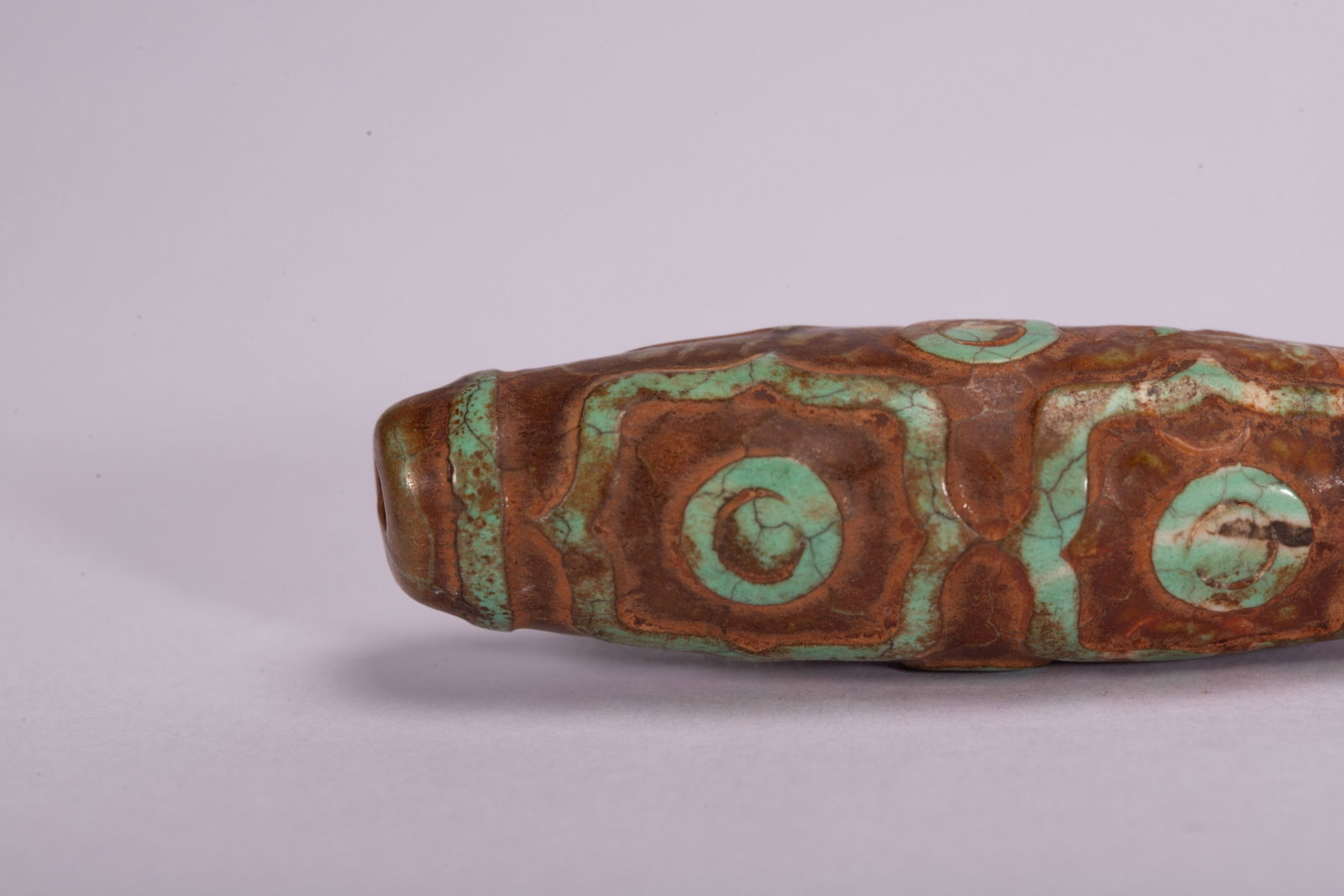 Chinese Turquoise-Inlaid Dzi Bead: Chinese Turquoise-Inlaid Dzi Bead This distinctive dzi bead measures 5.5 cm in length and weighs 20 grams. The elongated stone bead features a rich, earthy brown base, adorned with striking turquoise-