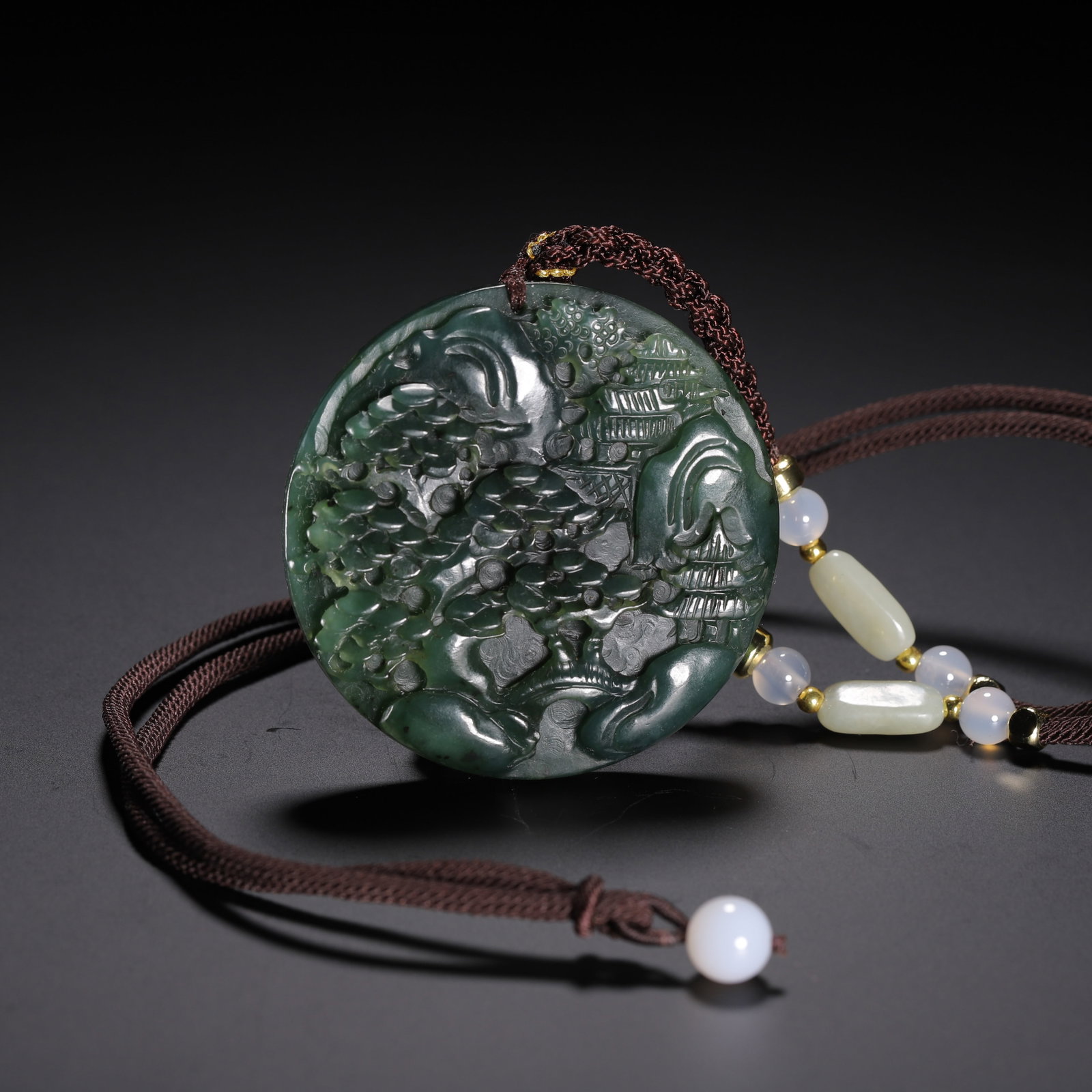 Chinese Spinach Jade Landscape Pendant: Chinese Spinach Jade Landscape Pendant A finely carved circular pendant made from rich spinach-green jade, depicting a serene landscape scene in deep relief. The carving features pavilions nestled amo