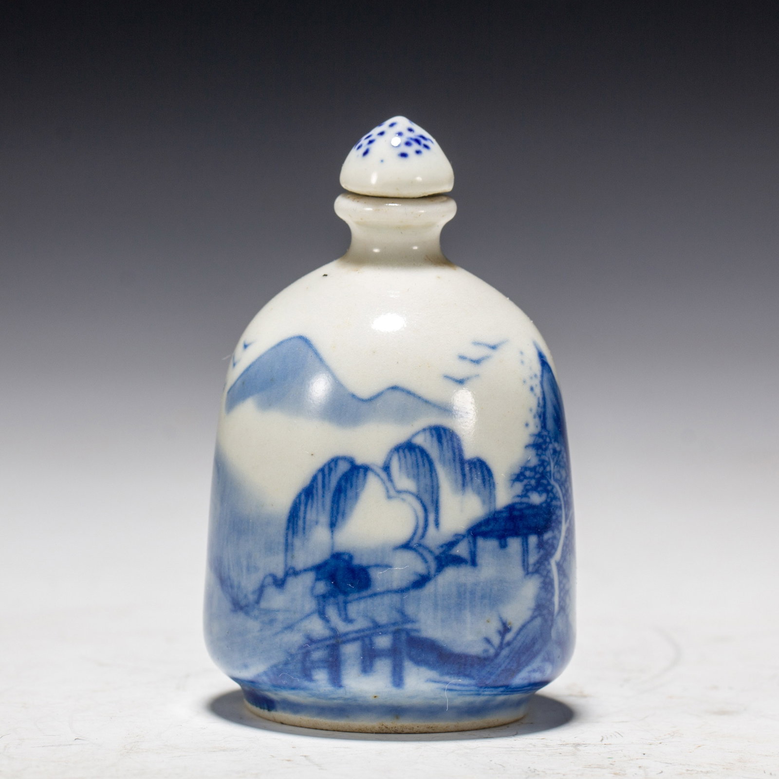 Chinese Blue and White Landscape Snuff Bottle: Chinese Blue and White Landscape Snuff Bottle A small porcelain snuff bottle painted in cobalt blue with a delicate landscape scene, depicting mountains, willow trees, a pavilion, and a figure