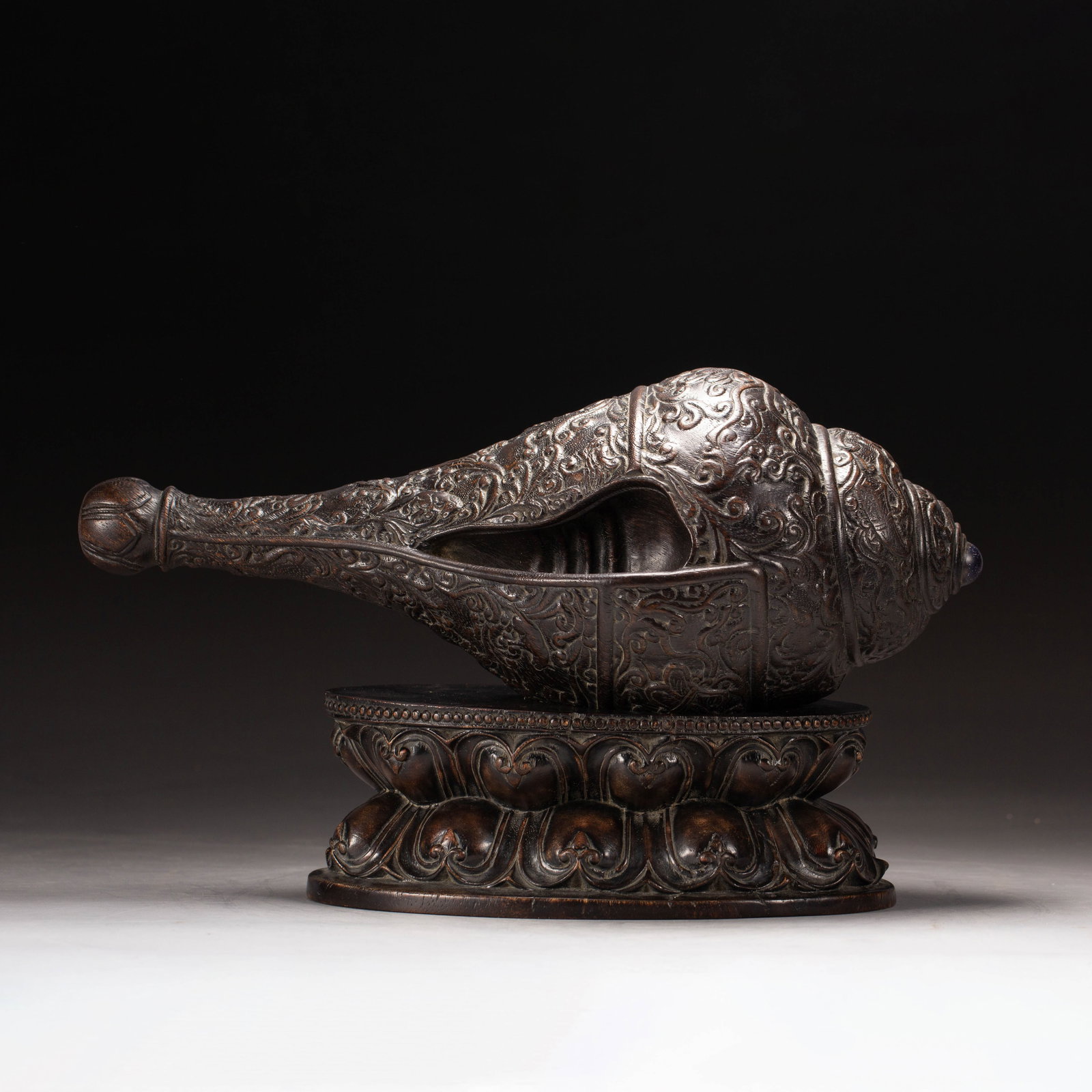 Chinese Agarwood Carved Buddhist Conch with Stand: Chinese Agarwood Carved Buddhist Conch with Stand A finely carved agarwood Buddhist conch, intricately decorated with deep relief floral and scrollwork patterns across its entire surface. The conch
