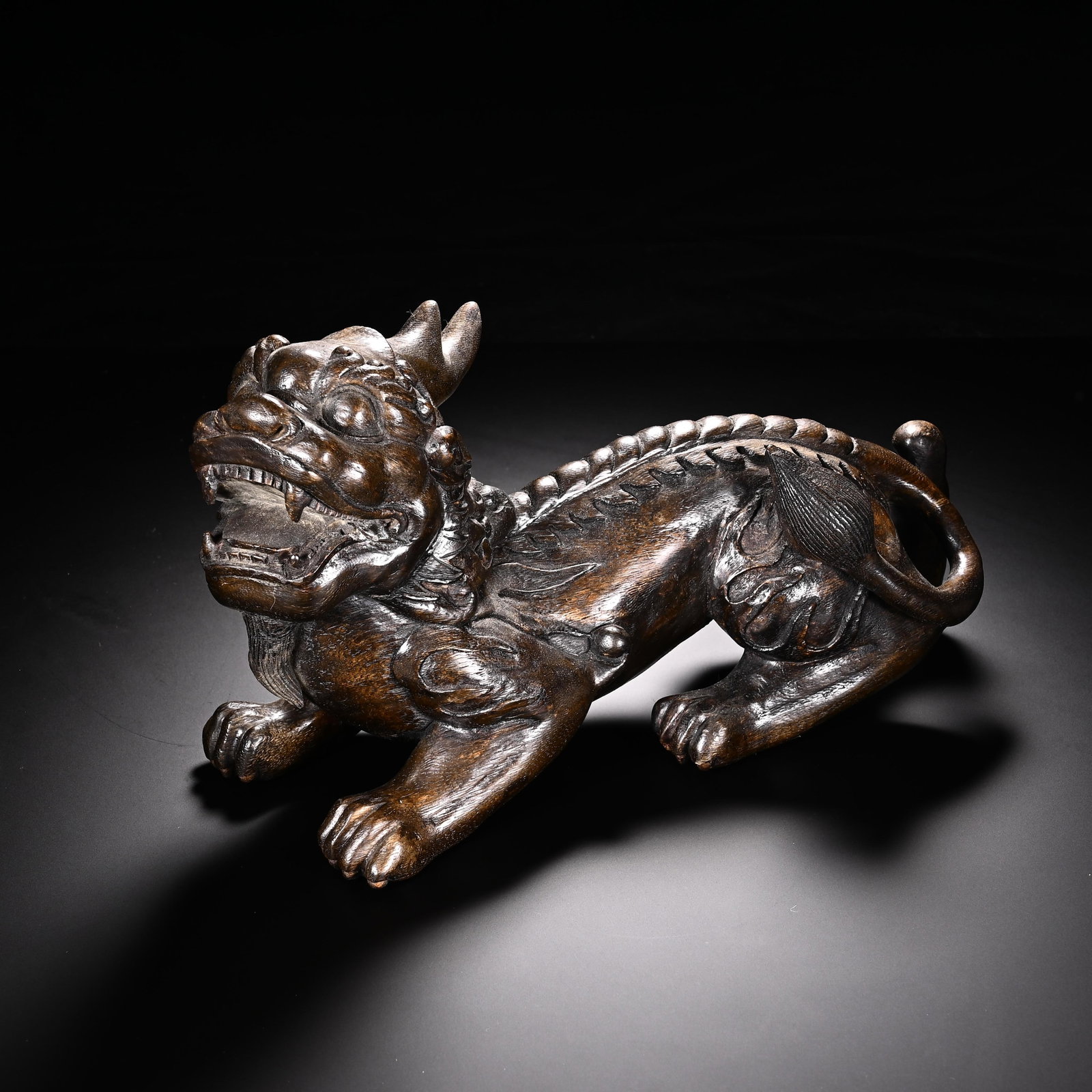 A Chinese Chenxiang Wood Mythical Beast: A Chinese Chenxiang Wood Mythical Beast A Chinese chenxiang wood carving of a mythical beast, likely a pixiu, carved in a recumbent pose with its mouth open in a roar. Its form is rendered with powerf
