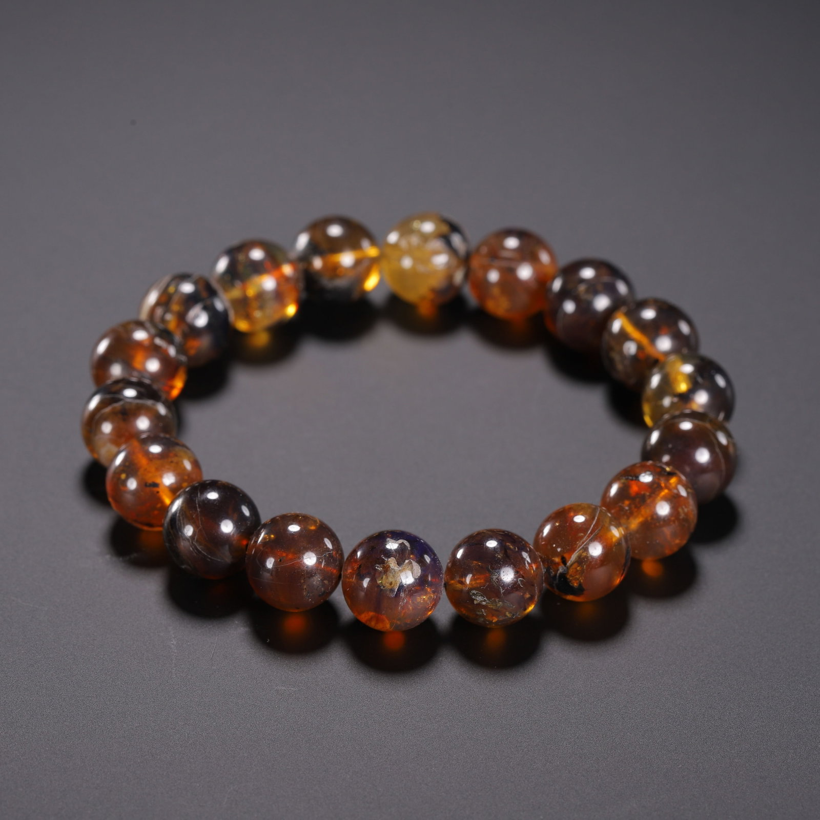 Chinese Amber Beaded Bracelet: Chinese Amber Beaded Bracelet A single strand bracelet composed of smooth, round amber beads, exhibiting a rich palette of warm hues from deep cognac to translucent golden-yellow. The beads show natur