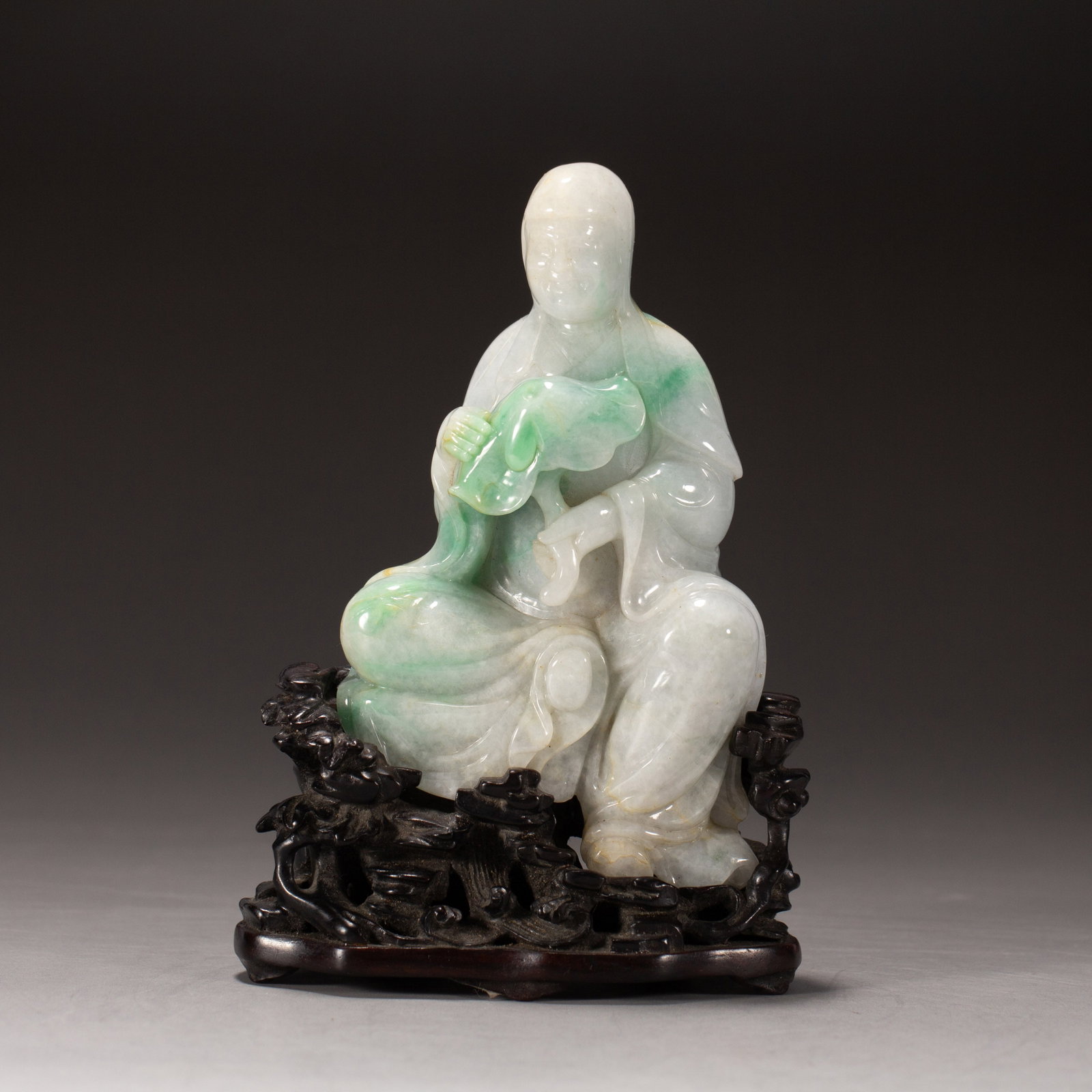 Chinese Jadeite Seated Luohan Ornament: Chinese Jadeite Seated Luohan Ornament A finely carved jadeite figure of a seated Luohan, rendered in translucent pale white stone with vivid green inclusions. The serene figure holds a leaf-shaped